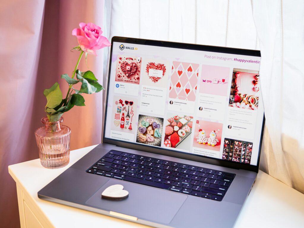A stylish workspace featuring a laptop with Valentine's Day visuals and a pink rose vase for a romantic touch.
