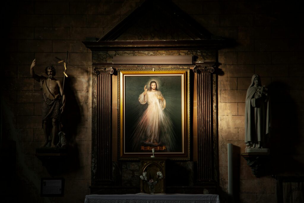 A framed religious portrait flanked by statues inside a dimly lit French church.