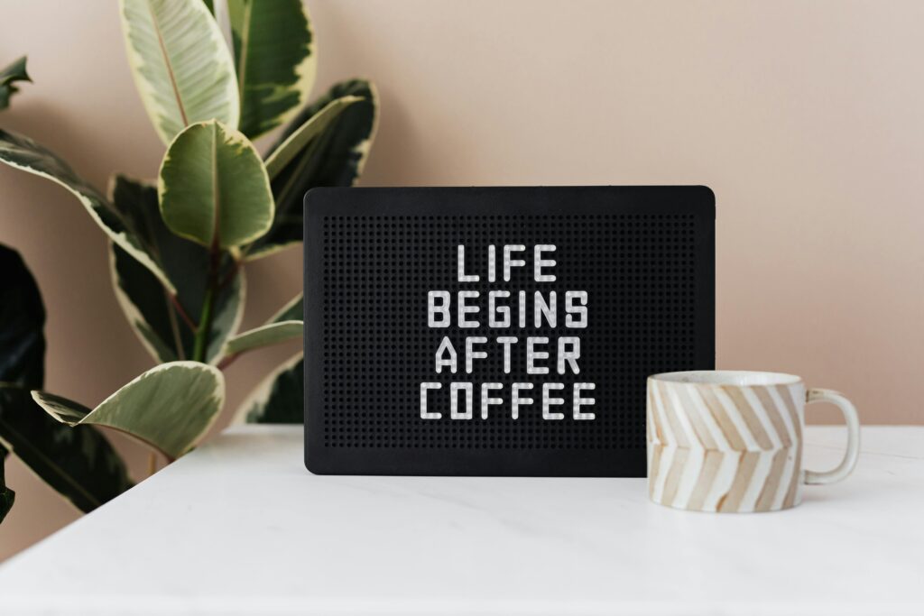 Motivational coffee sign with a potted plant and decorative mug on a table.