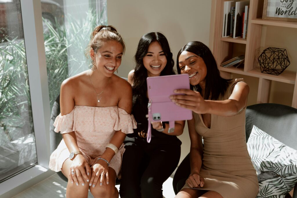 A group of happy young women bonding and laughing while looking at a tablet indoors.
