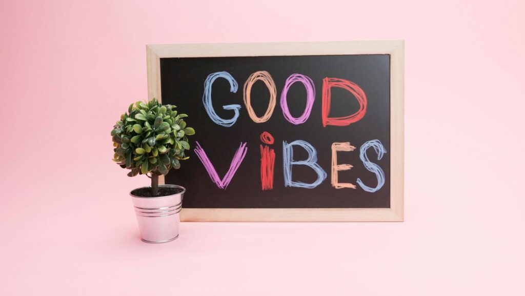 Chalkboard with 'Good Vibes' in colorful letters against a pink background with a potted plant.
