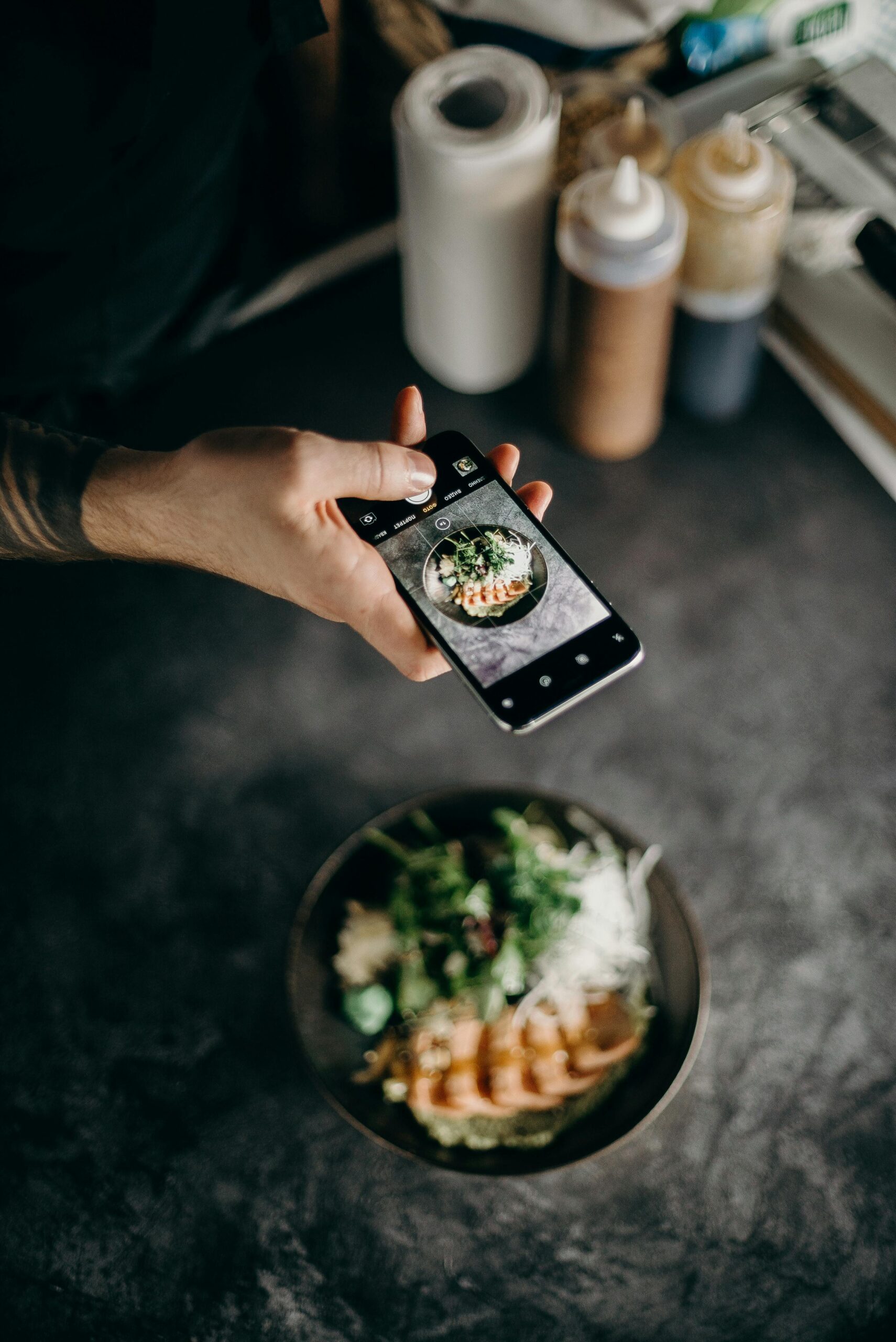 A person photographing a beautifully plated Asian dish with a smartphone camera.