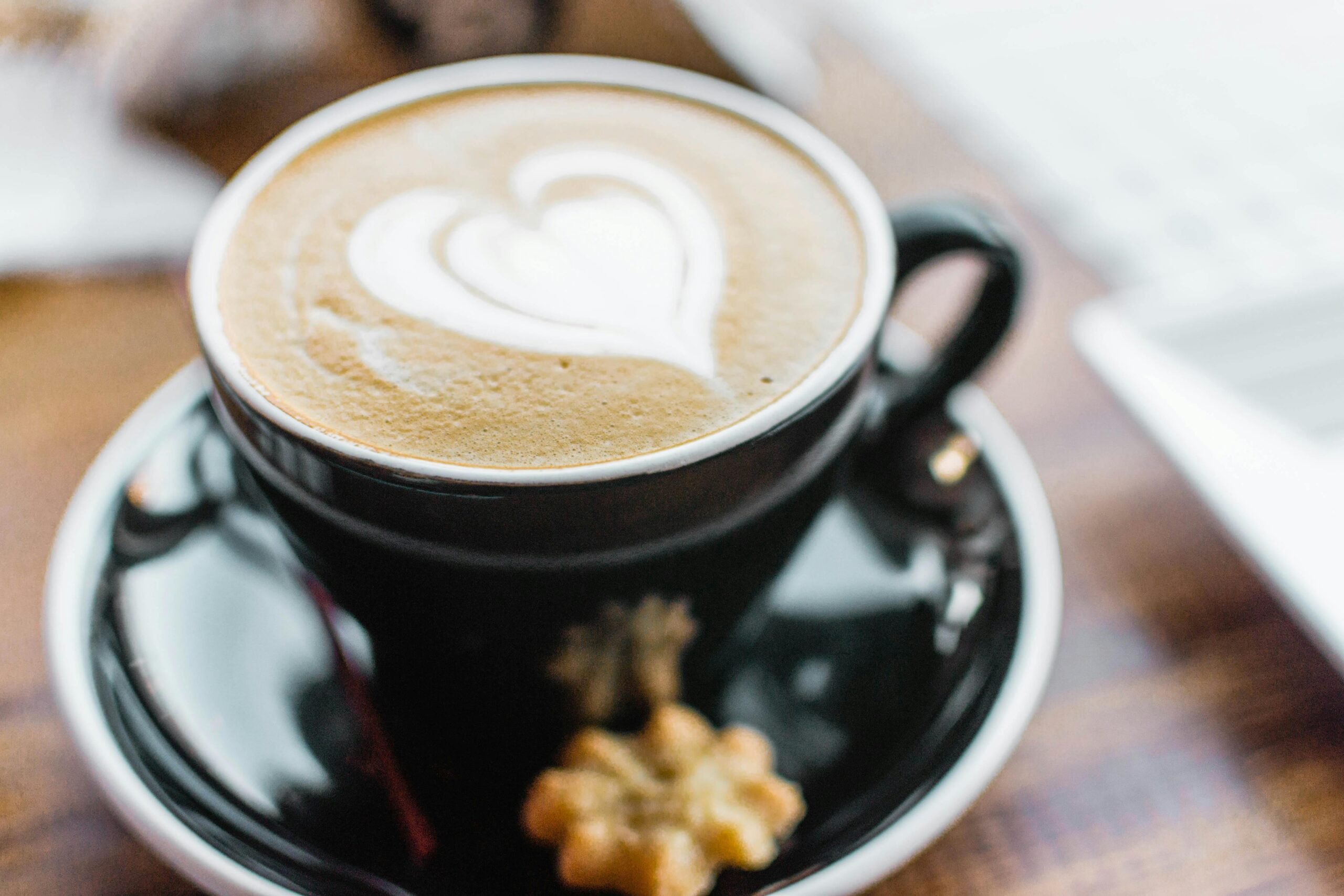 Close-up of a heart-shaped latte art in a black cup with saucer on a wooden table.